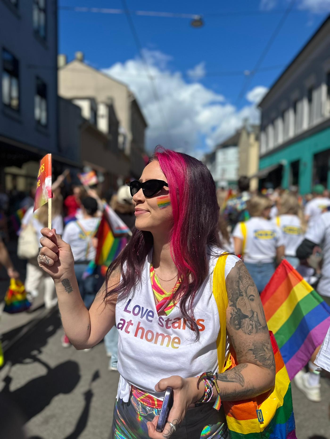 En IKEA ansatt på PRIDE-parade som være IKEA STORSTOMMA pose og vifter et flagg.