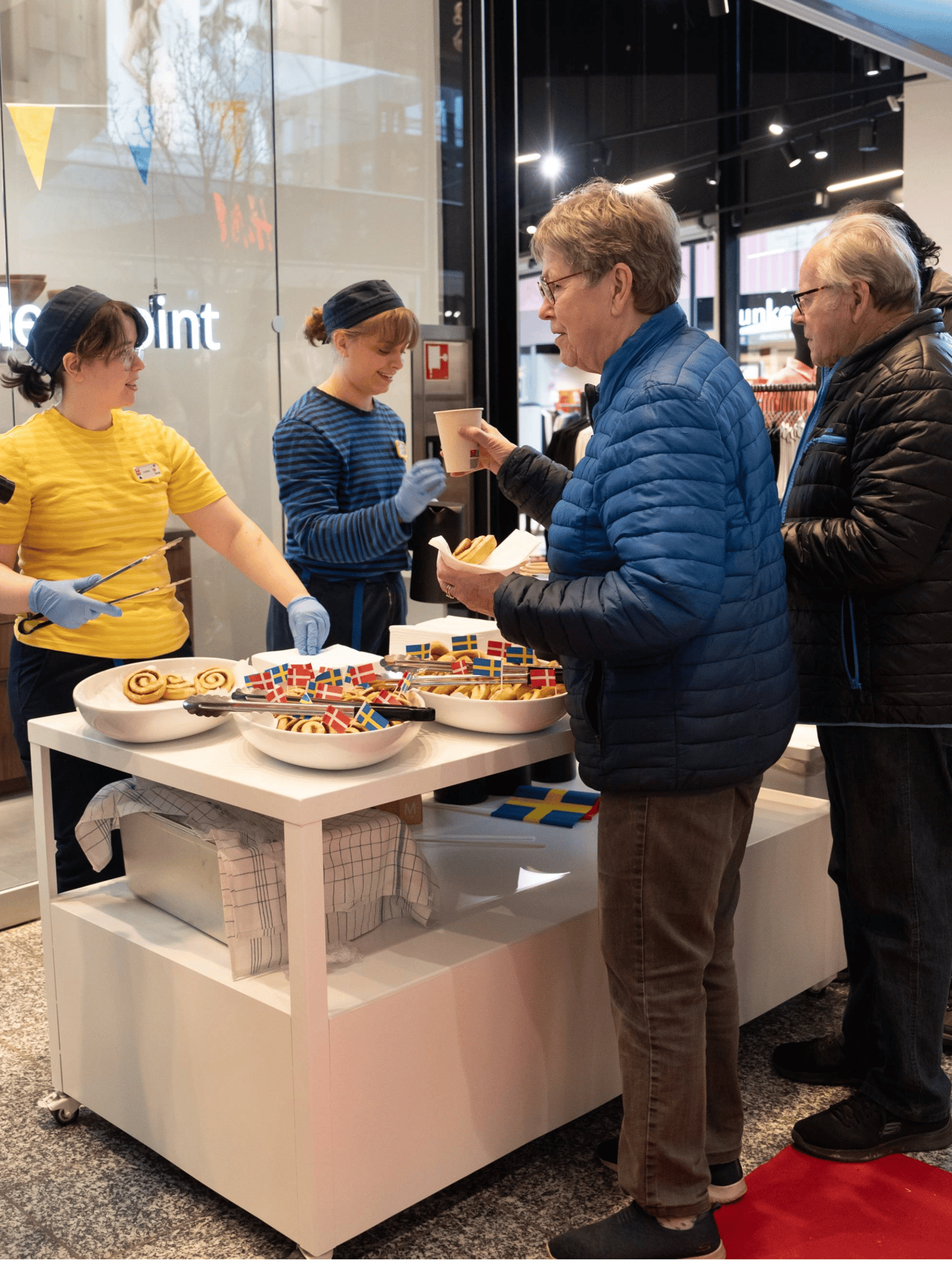 En IKEA medarbejder i sin uniform serverer kage til fremmødte gæster ude foran IKEA Plan and Order Point Herning.