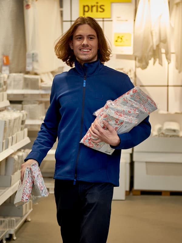 En IKEA medarbejder smiler glad mens han kommer bærende på en stak sengetøj i et IKEA varehus.