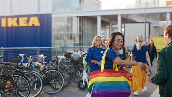 En IKEA medarbejder står foran IKEA København ved åbningen og deler gaver ud til forbipasserende over skulderen har hun en regnbuefarvet IKEA bærepose.