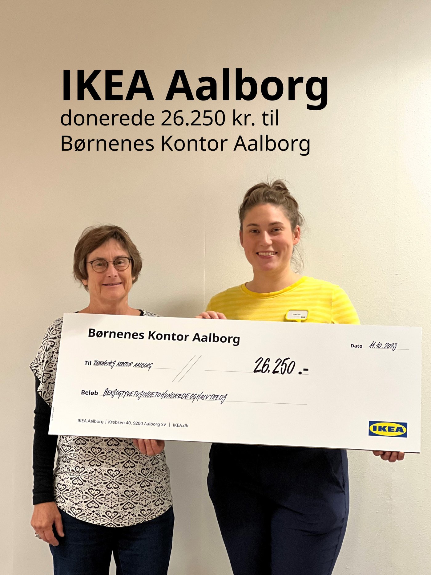 En IKEA medarbejder står sammen med en kvinde og holder en stor check øverst står der med sort skrift IKEA Ålborg donerede 26250 kroner til Børnenes Kontor Aalborg.
