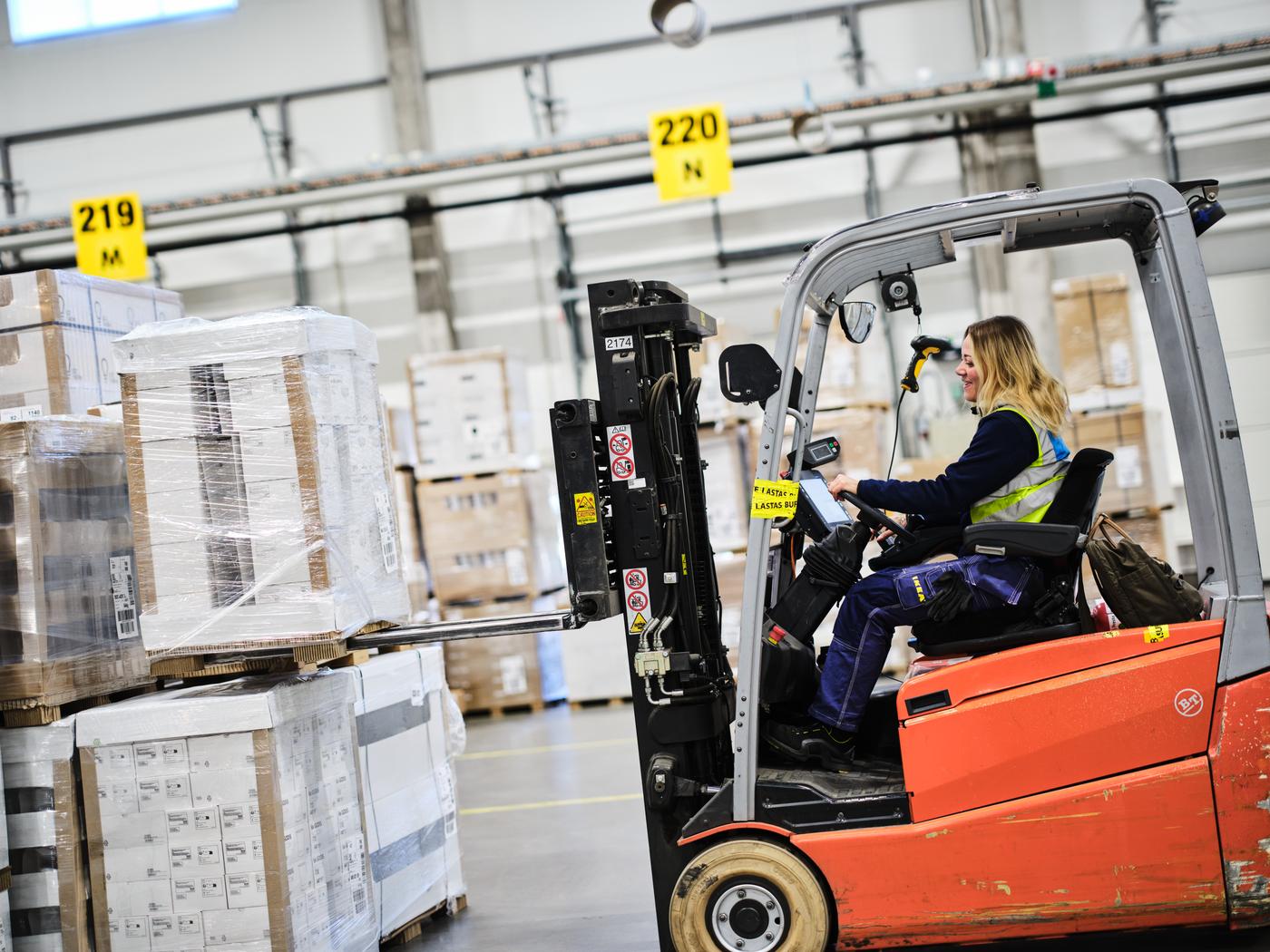 En IKEA medarbetare i ett lager kör en truck och lastar på en pall på trucken.