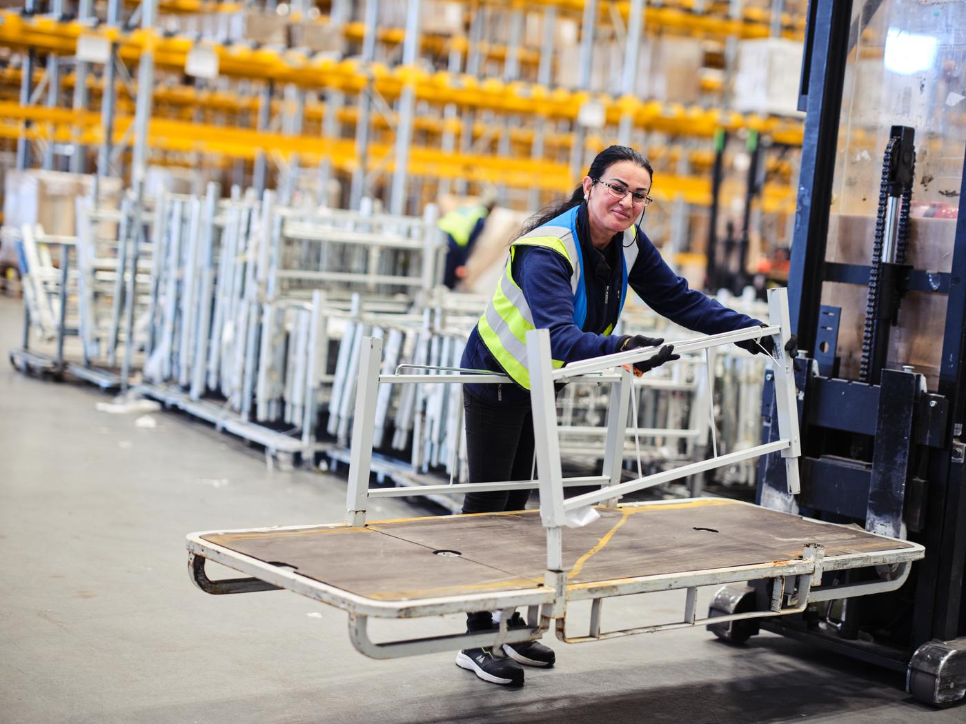 En IKEA medarbetare i ett lager lastar en ställning på en truck. Personen tittar upp och ler mot kameran.