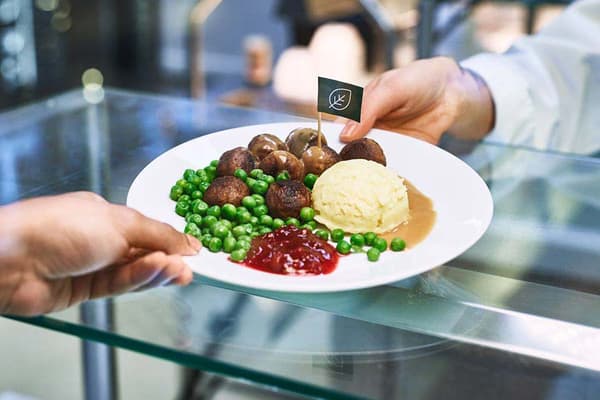 En IKEA medarbetare i resturangen som ger en kund IKEA vego köttbullar.