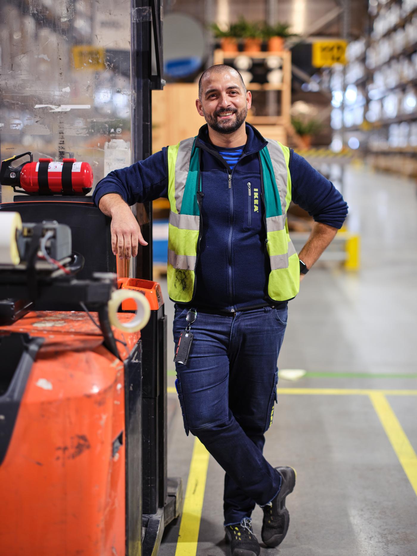 En IKEA medarbetare klädd i arbetskläder och säkerhetsväst står och lutar sig mot en truck samtidigt som han ler mot kameran.
