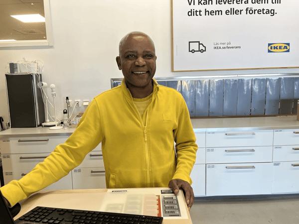 En IKEA medarbetare står vid ett skrivbord och ler mot kameran.