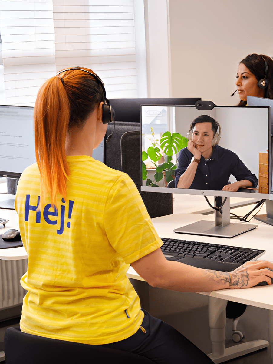 En IKED medarbetare står vid ett skrivbord. Man ser hennes rygg där det står "Hej!".