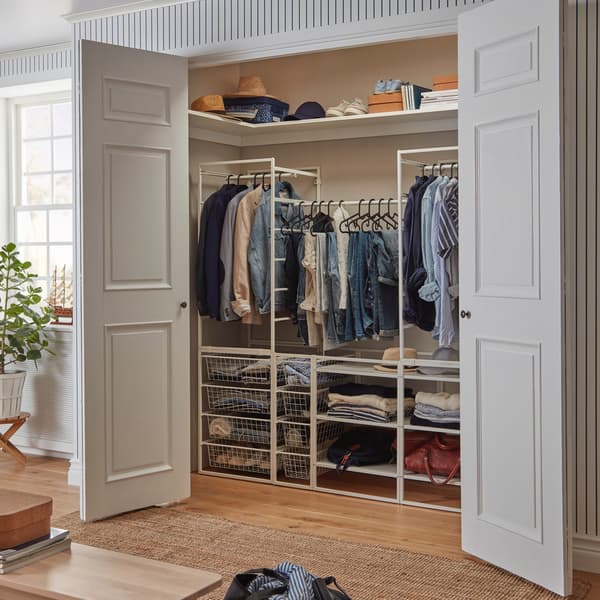 En JONAXEL kombination med garderobestænger, trådkurve og hylder, der bruges som et walk-in-closet i et lille rum bag grå dobbeltdøre.