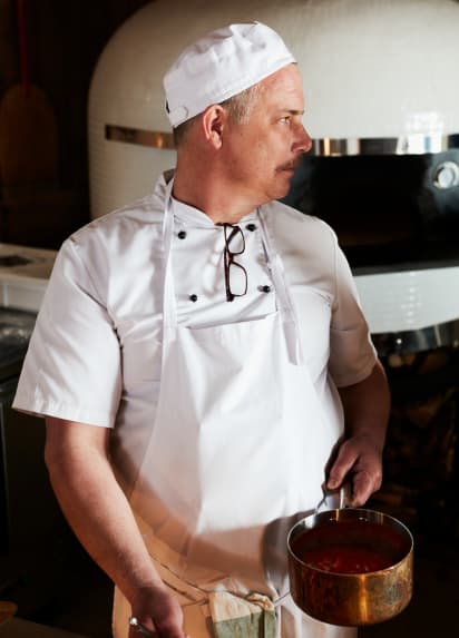 En kokk med en kobbergryte i hånda.