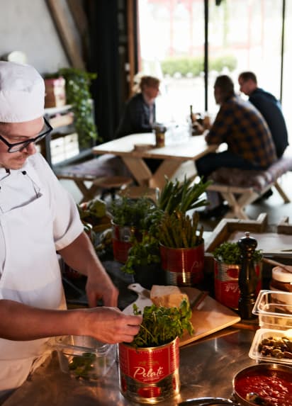 En kokk tilbereder pizza i et åpen kjøkkenlandskap i restauranten.