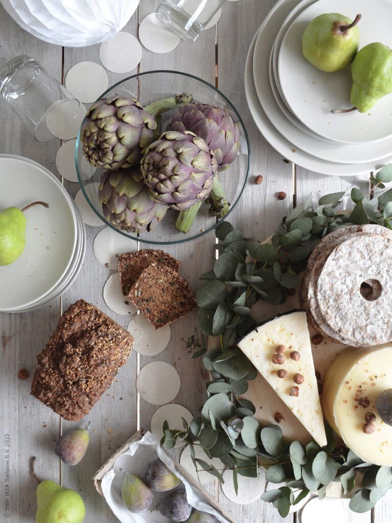 En kronärtskocka och bröd ligger bredvid ostar på ett bord.