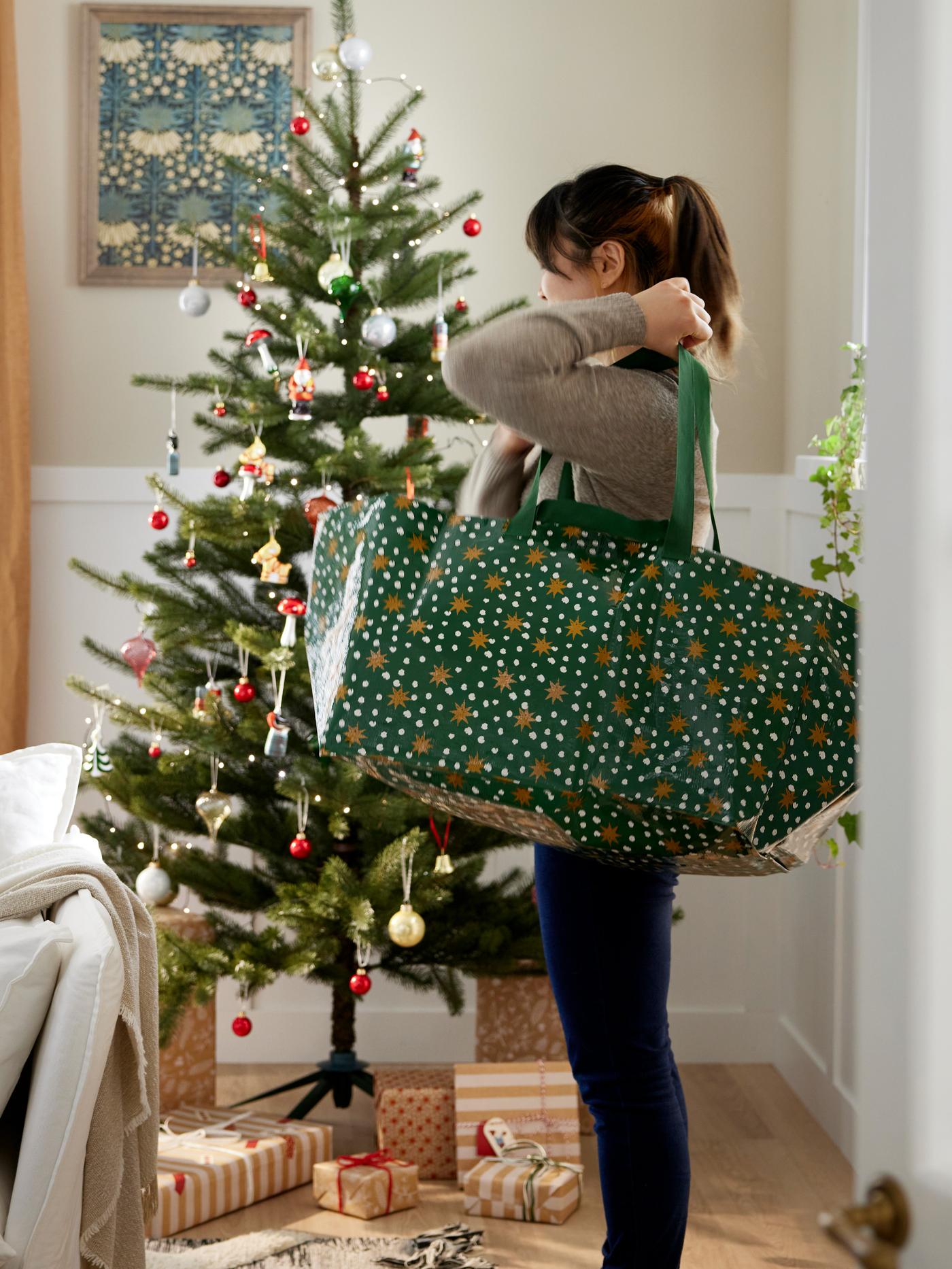En kvinde bærer en IKEA FRAKTA bærepose på skulderen og står foran et pyntet juletræ.