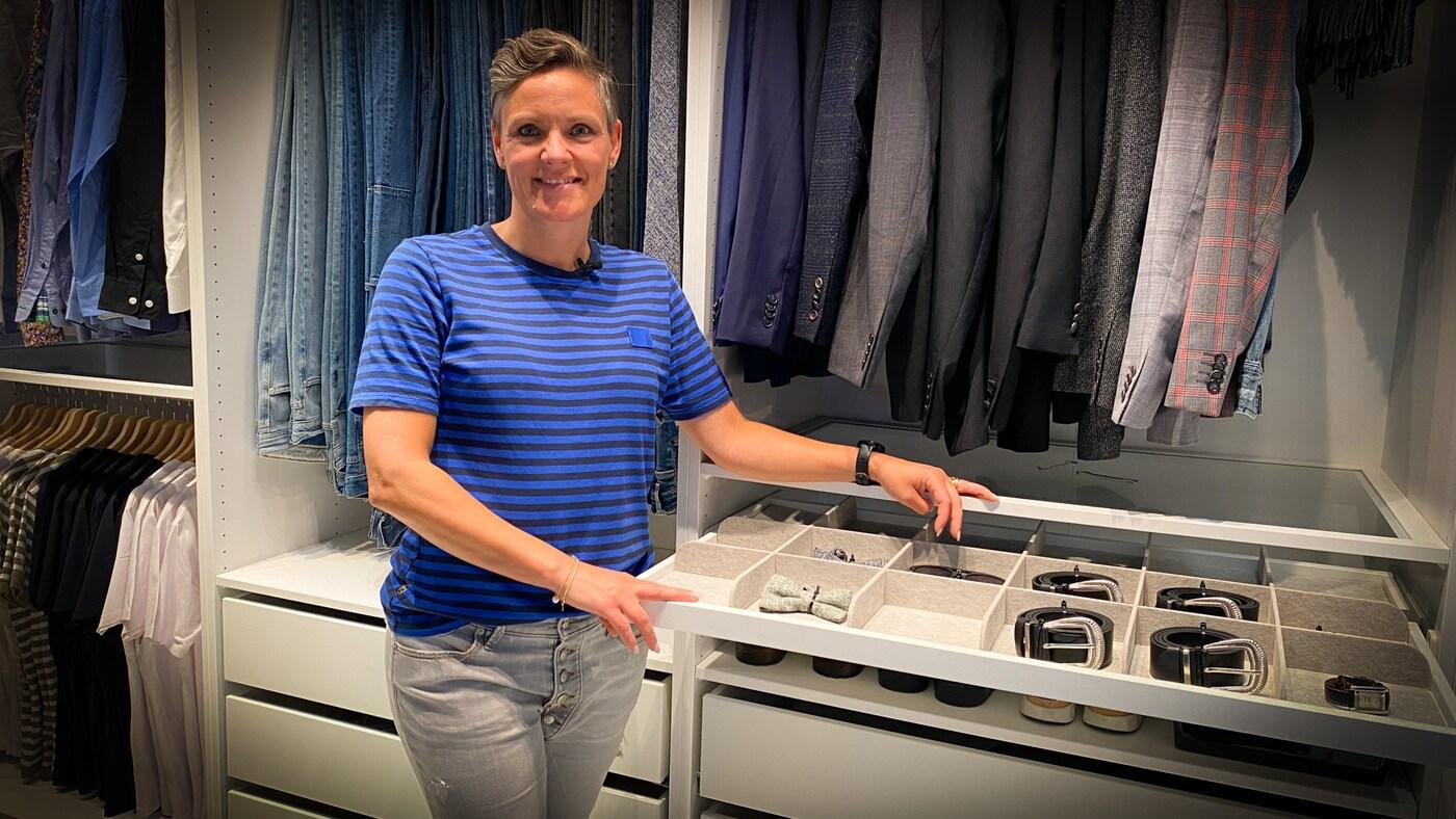 En kvinde i en blå T-shirt står foran et stort, åbent og velorganiseret klædeskab.