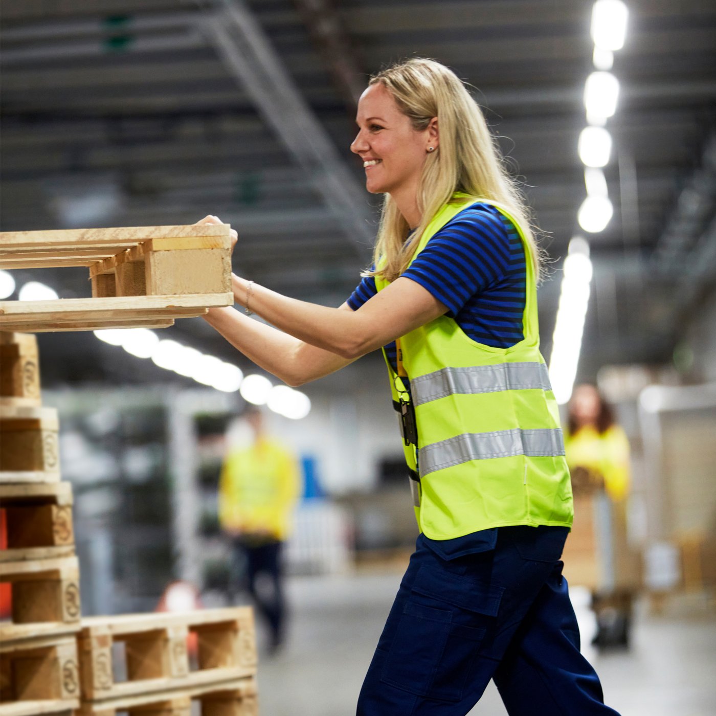 En kvinde i gul refleksvest og IKEA t-shirt skubber en palle ind på plads.
