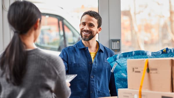 En kvinde med ryggen til afleverer papirer til en smilende IKEA medarbejer og til højre i billedet kan ses flere IKEA pakker og en blå IKEA pose.