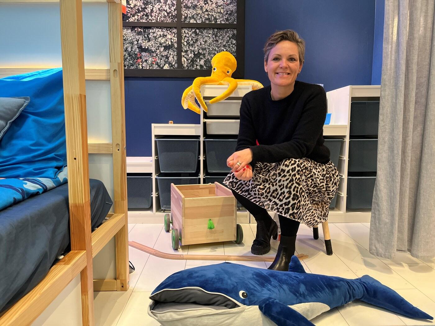 En kvinde sidder på en taburet i et børneværelse med TROFAST opbevaring i baggrunden.