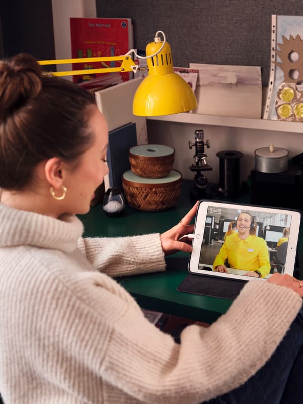 En kvinde sidder ved et skribebord med en tablet og taler med en IKEA medarbejder online.