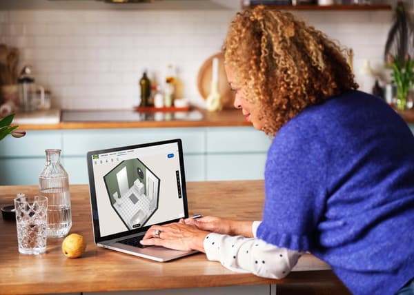 En kvinde står ved et køkkenbord og tegner et badeværelse på sin computer.