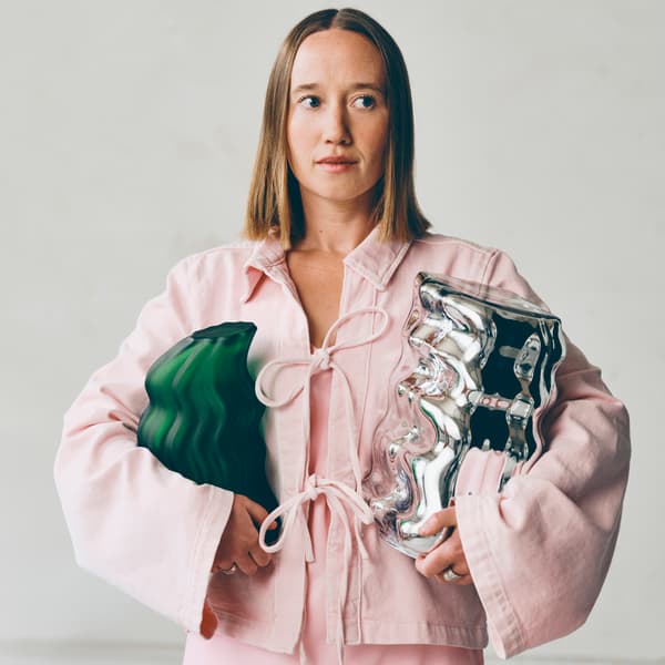 En kvinna i rosa kavaj håller i två konstföremål.