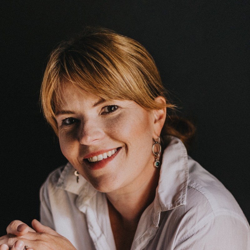 En kvinna med en vit blus står mot en svart vägg.