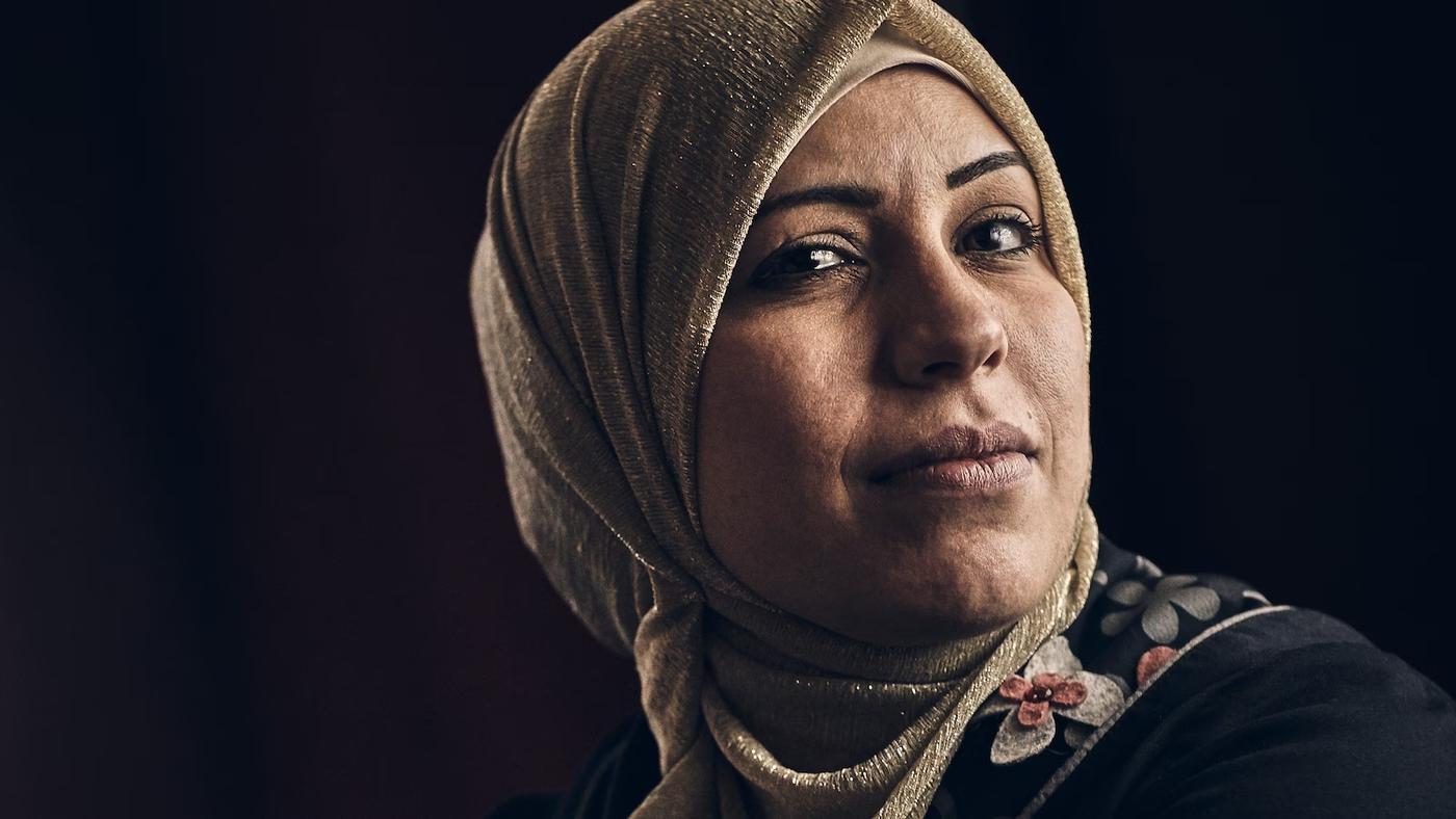 En kvinna med hijab som kollar in i kameran och småler.