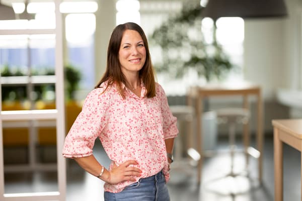 En kvinna med mörkt hår står i ett kontorslandskap. 