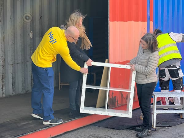 En kvinna och man tar emot en vit bokhylla som lyfts in i containern av en kvinna