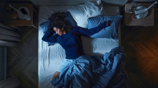 En kvinna sover i en säng med blå sängkläder.