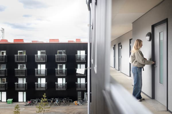 En kvinna står på en loftgång och låser upp dörren till sin lägenhet. 