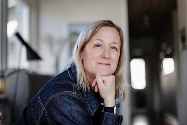 En kvinna stöder hakan mot höger hand och blickar framåt.
