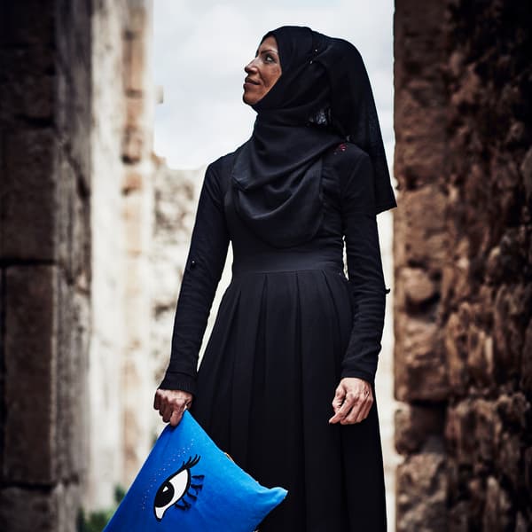 En kvinnelig palestinsk flyktning og håndverker holder i ei blå pute med store øyne på som hun har laget til en IKEA-kolleksjon.