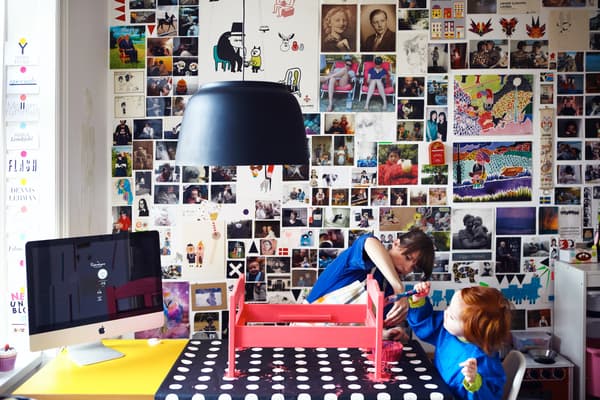  En la mitad inferior de la imagen aparecen una mujer y un niño con poleras azules pintando una caja roja posada sobre una mesa con un mantel negro con puntos blancos. 