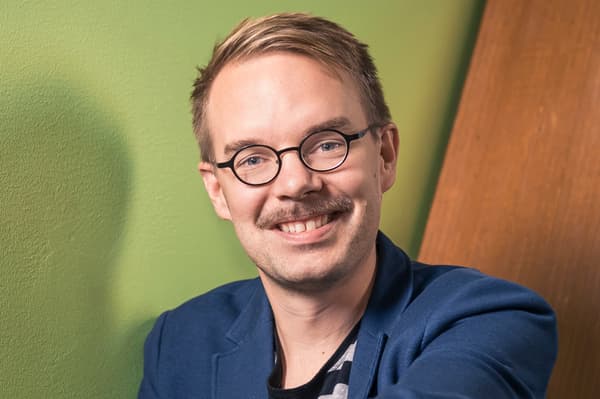 En ljushårig man i glasögon ler och tittar mot kameran.
