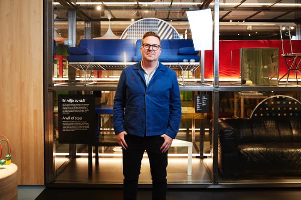 En man i blå jacka och mörka byxor står framför en utställning med IKEA-möbler. 