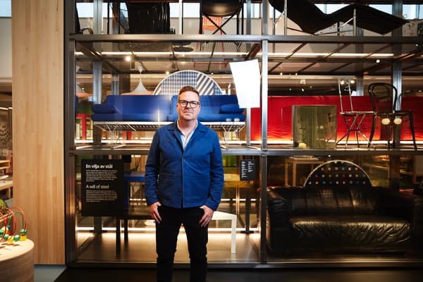 En man i blå jacka och mörka byxor står framför en utställning med IKEA-möbler.