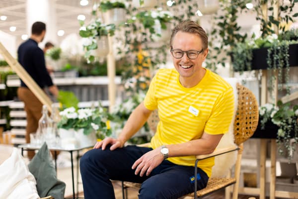 En man i glasögon och gul tröja står lutad mot hylla och ler mot kameran