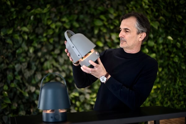 En man i svart polotröja håller uppe en vit lyktainspirerad lampa. En likadan lampa i blått står bredvid