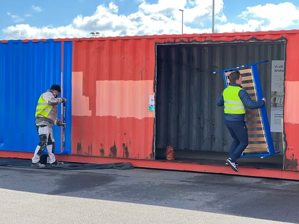 En man målar container i blå förg medan en kvinna bär in på en blåmålad säng