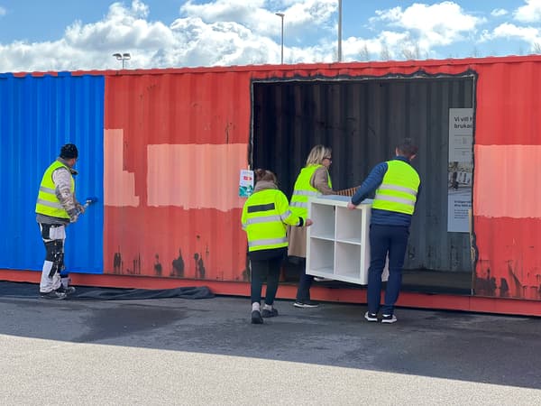 En man målar en container blå medan tre personer hjälps åt att bära in en vit bokhylla in i containern