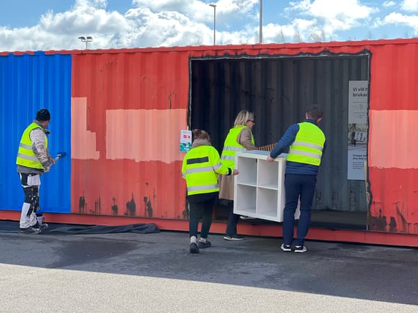 En man målar en container blå medan tre personer hjälps åt att bära in en vit bokhylla in i containern