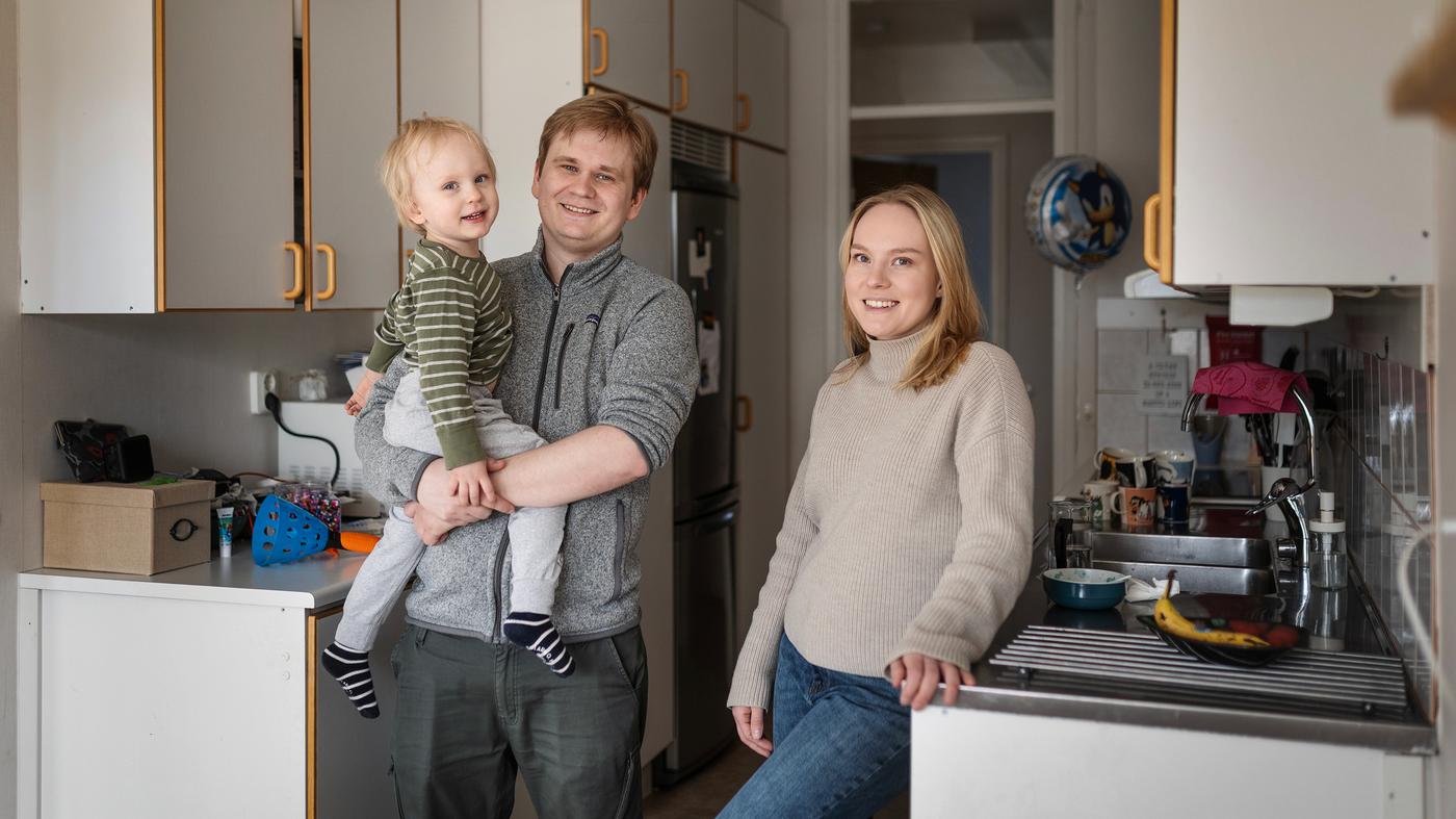 En man och en kvinna står i ett kök. Mannen håller ett barn i famnen. 