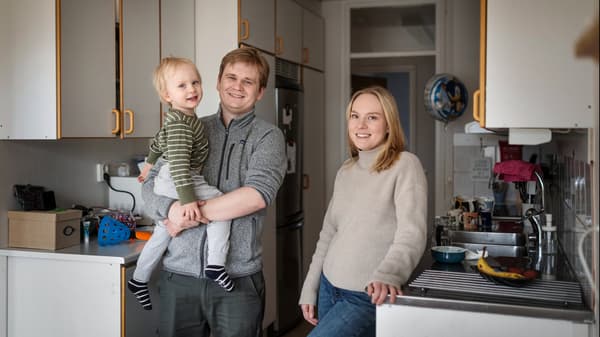 En man och en kvinna står i ett kök. Mannen håller ett barn i famnen. 