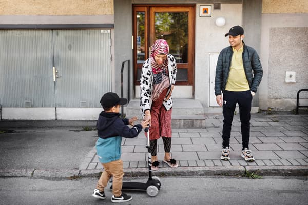 En man och en kvinna står på en trottoar. Kvinnan håller i en sparkcykel, som ett barn står bredvid. 