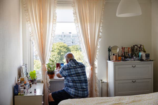 En man sitter vid ett fönster. Han tar bilder ut genom fönstret med sin mobiltelefon. 