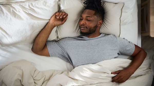 En man sover på rygg i en skön säng med gråbeige ÄNGSLILJA sängkläder
