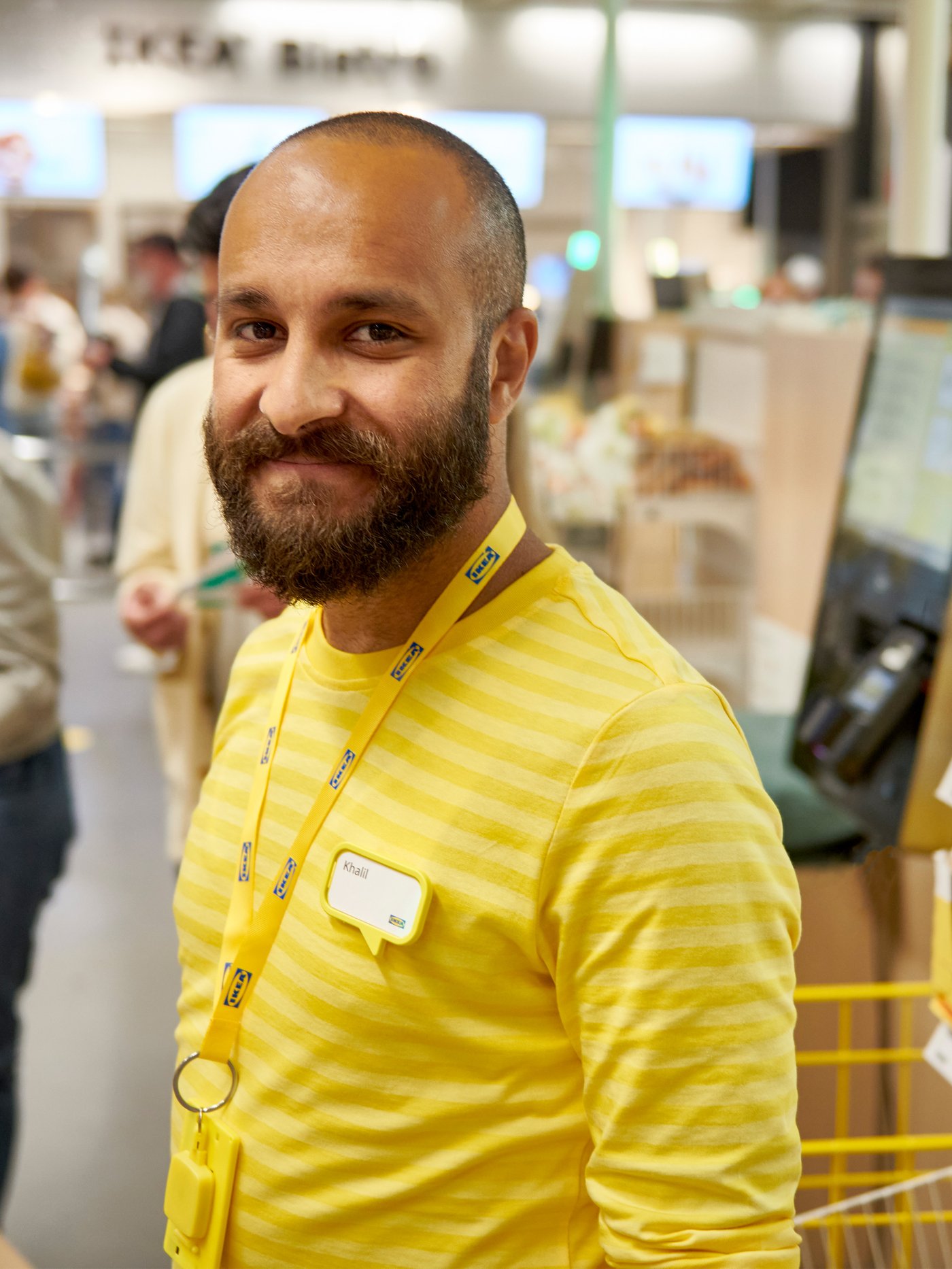 En mand i en gul IKEA uniform kigger ind i kameraet og smiler.