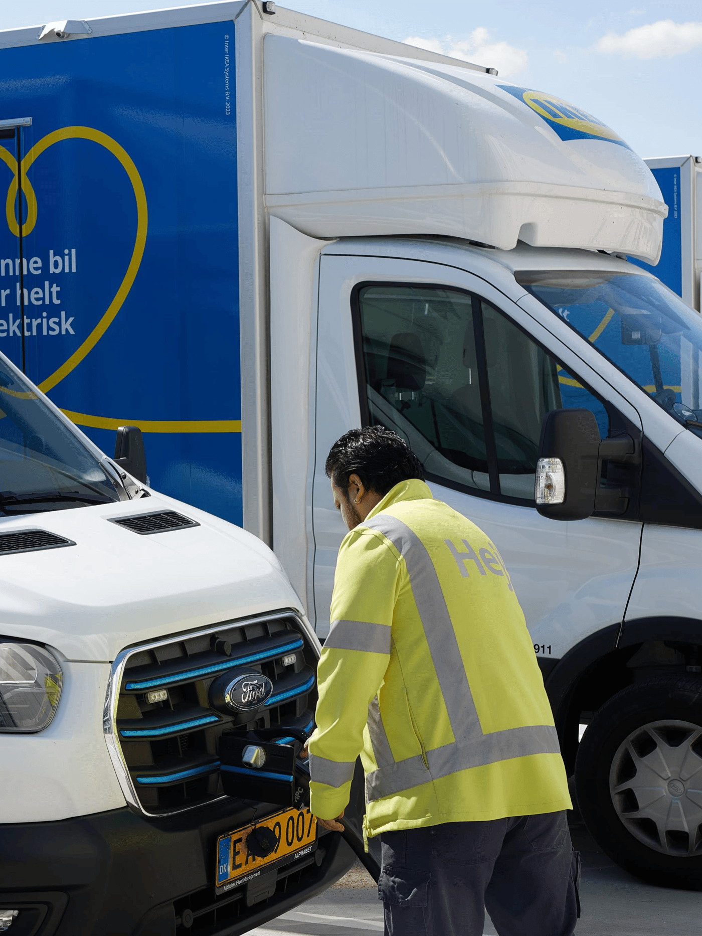 En mand i en refleksvest står foran køleren på en lastbil bag ham holder en anden lastbil.