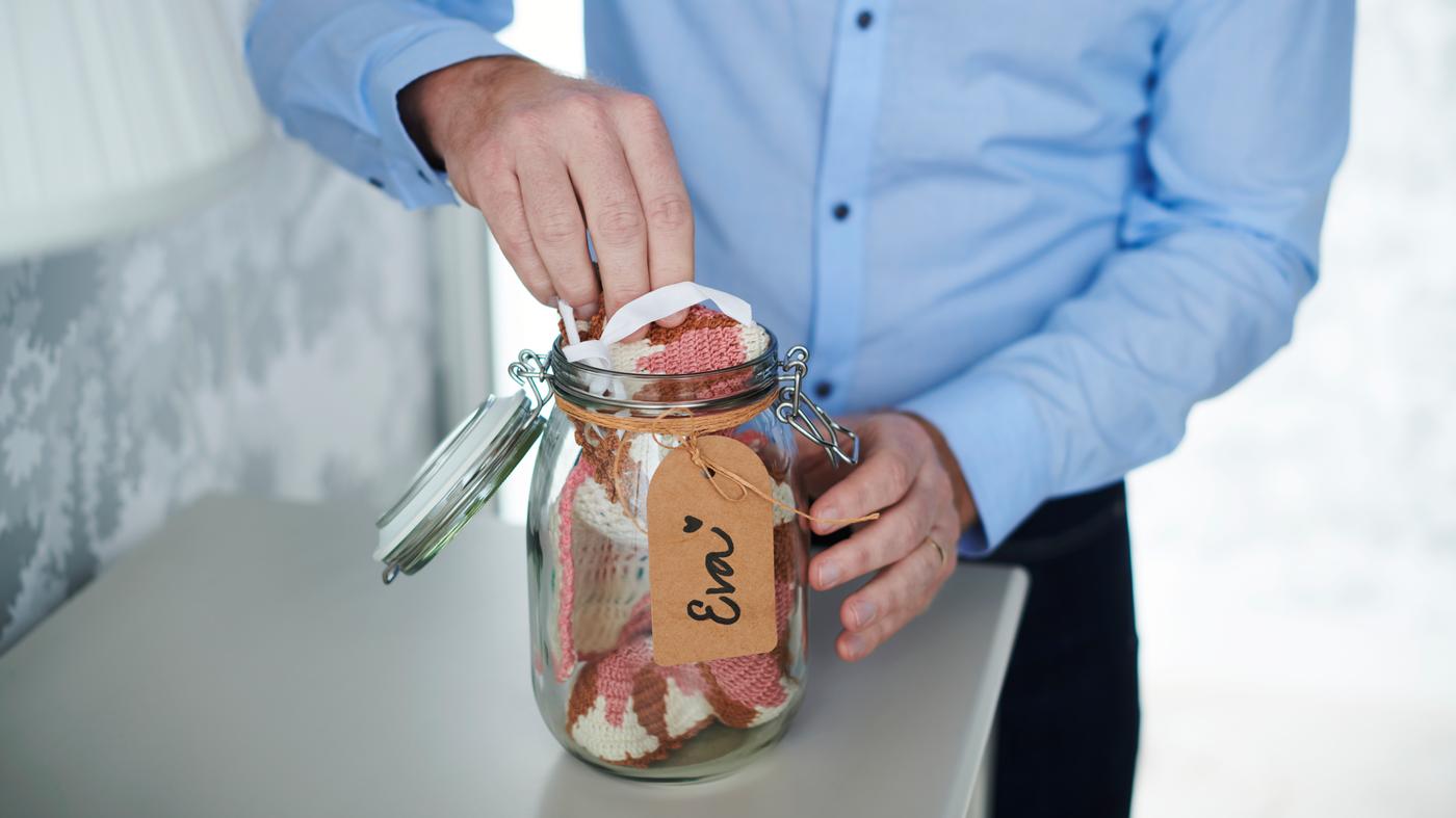 En mand i en skjorte lægger en hæklet klud i en KORKEN krukke af glas. Der er bundet en snor med et håndskrevet mærkat omkring krukkens hals.