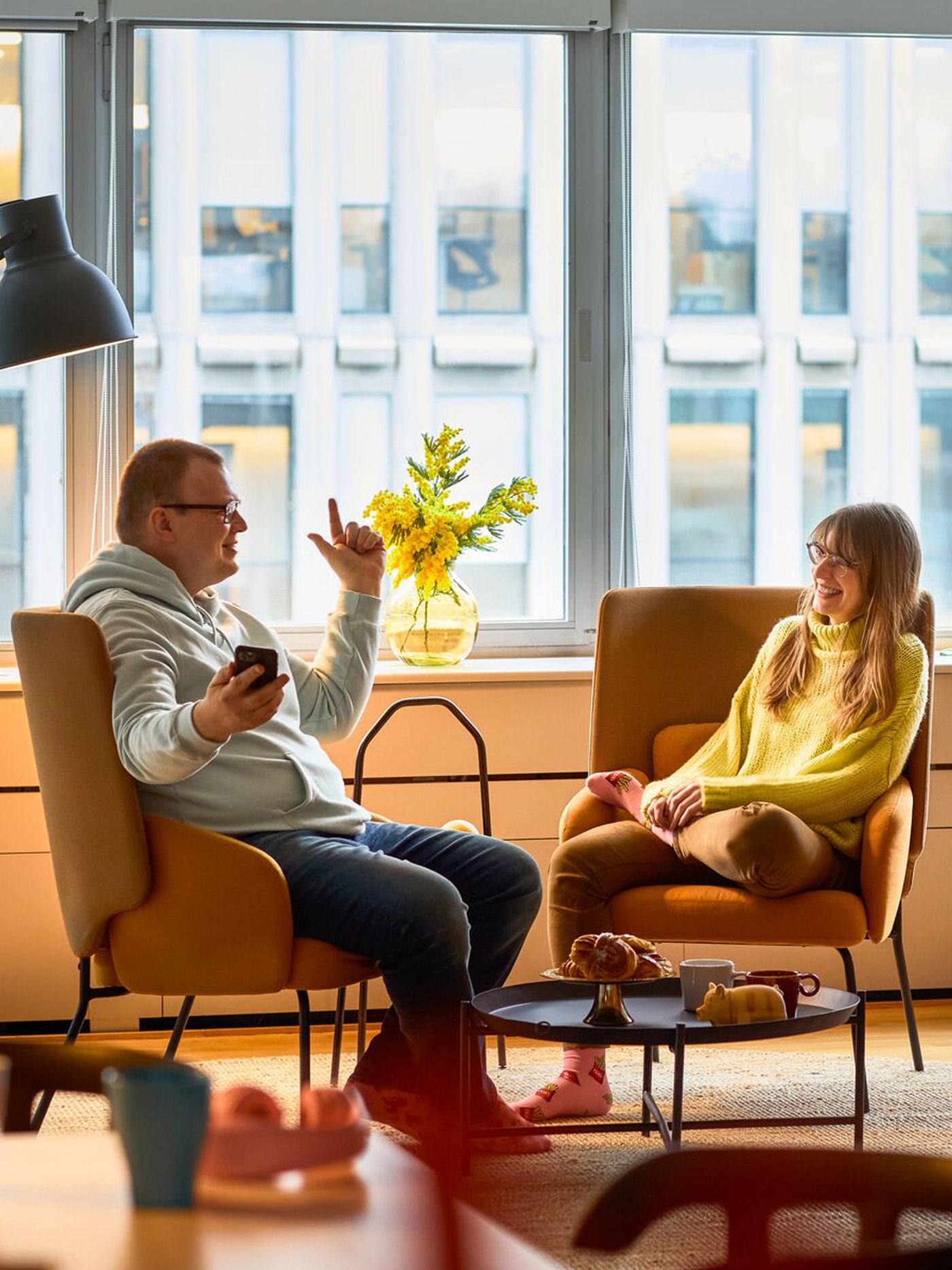 En mand og en kvinde sidder og taler i to gule lænestole foran et stort vindue.