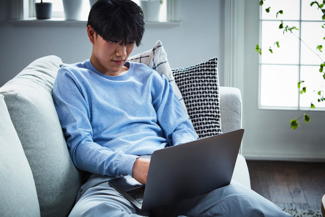 En mand sidder i en sofa med en bærbar computer.